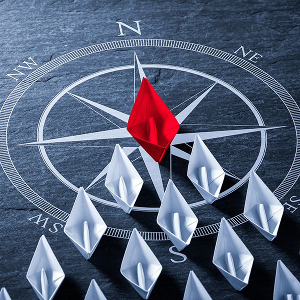 Red,Paper,Boat,On,Compass,Leading,A,Fleet,Of,Small